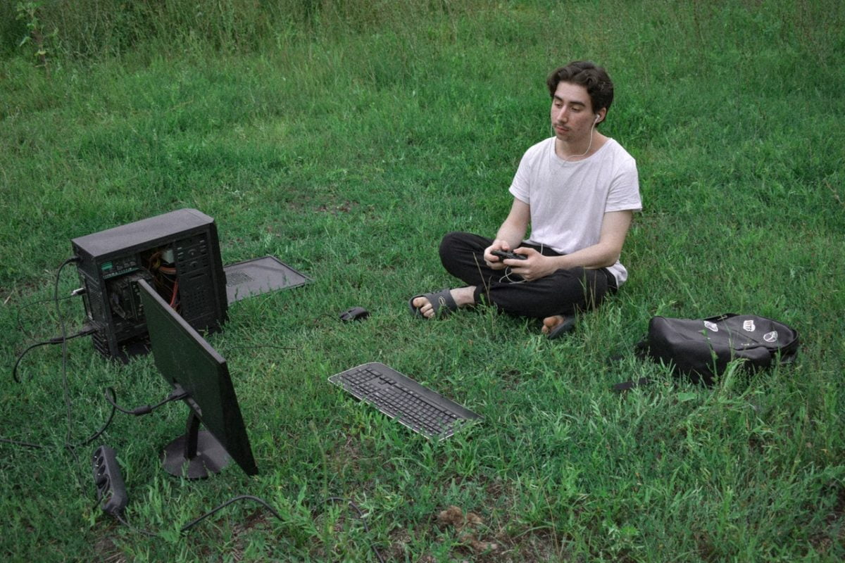 homme assis dans l'herbe face à un ordinateur