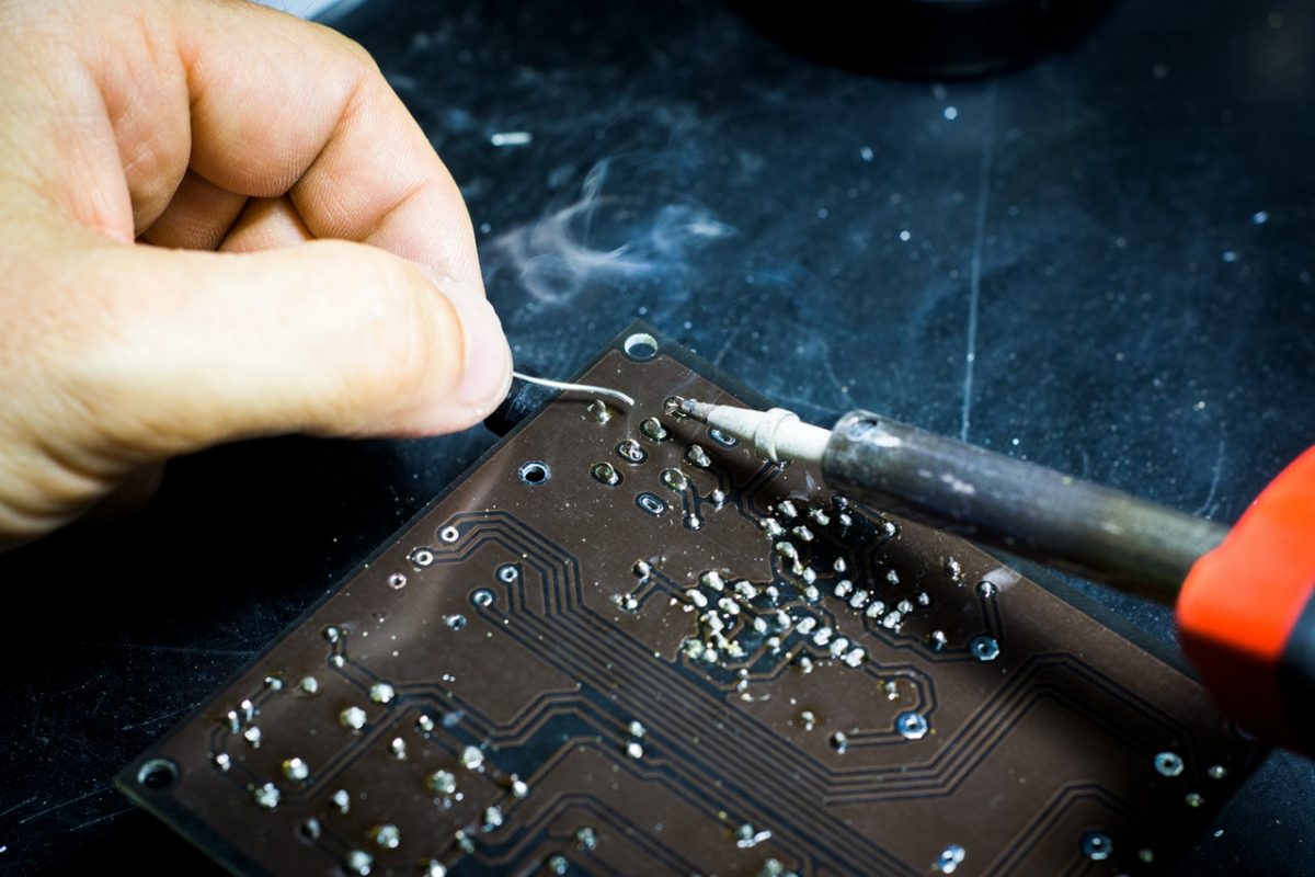 une personne avec un fer à souder réparer une carte électronique